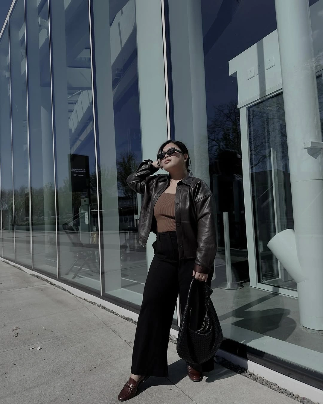 Short dark jacket over fitted brown top, black wide-leg trousers, and burgundy loafers