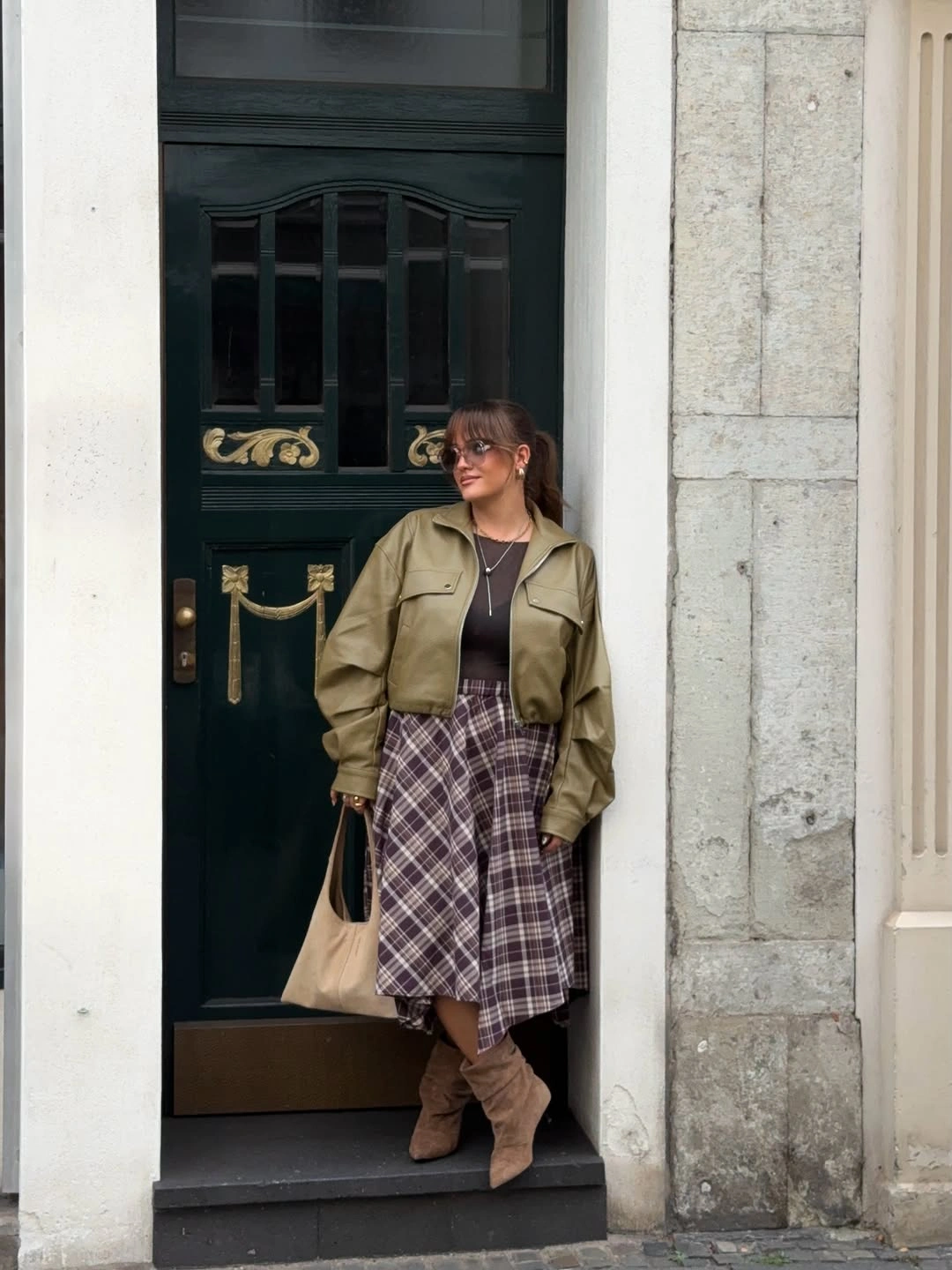 Olive pocketed jacket with brown top plaid midi skirt and tall boots