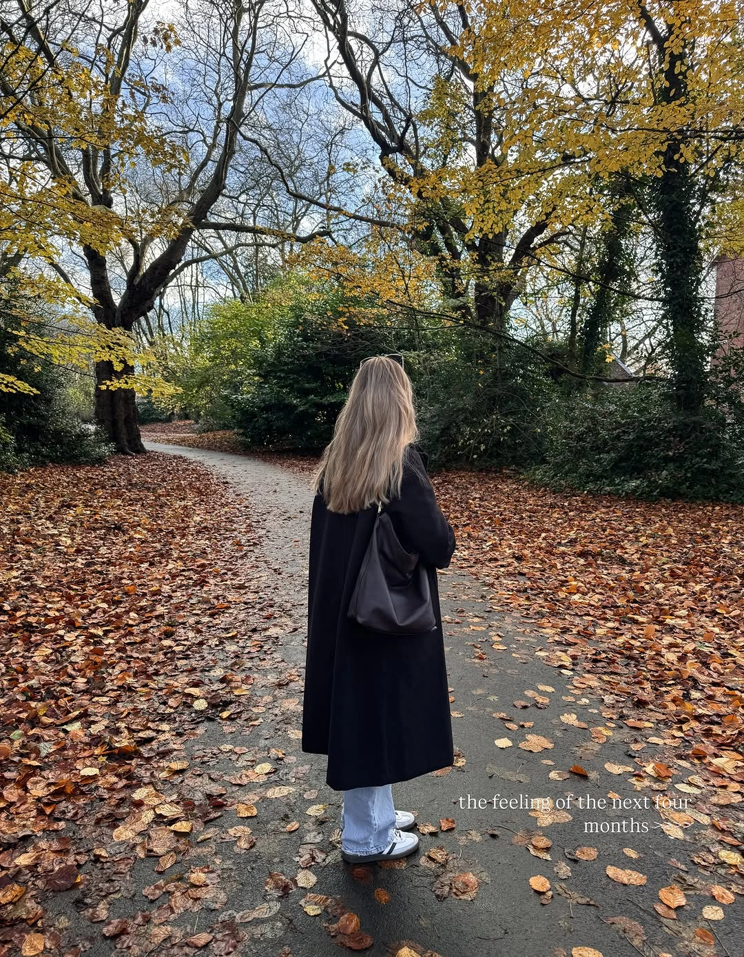 Long black coat light jeans sneakers and shoulder bag