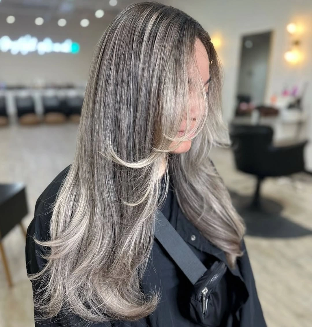 Long silver ash hair with darker gray strands and feathered face framing