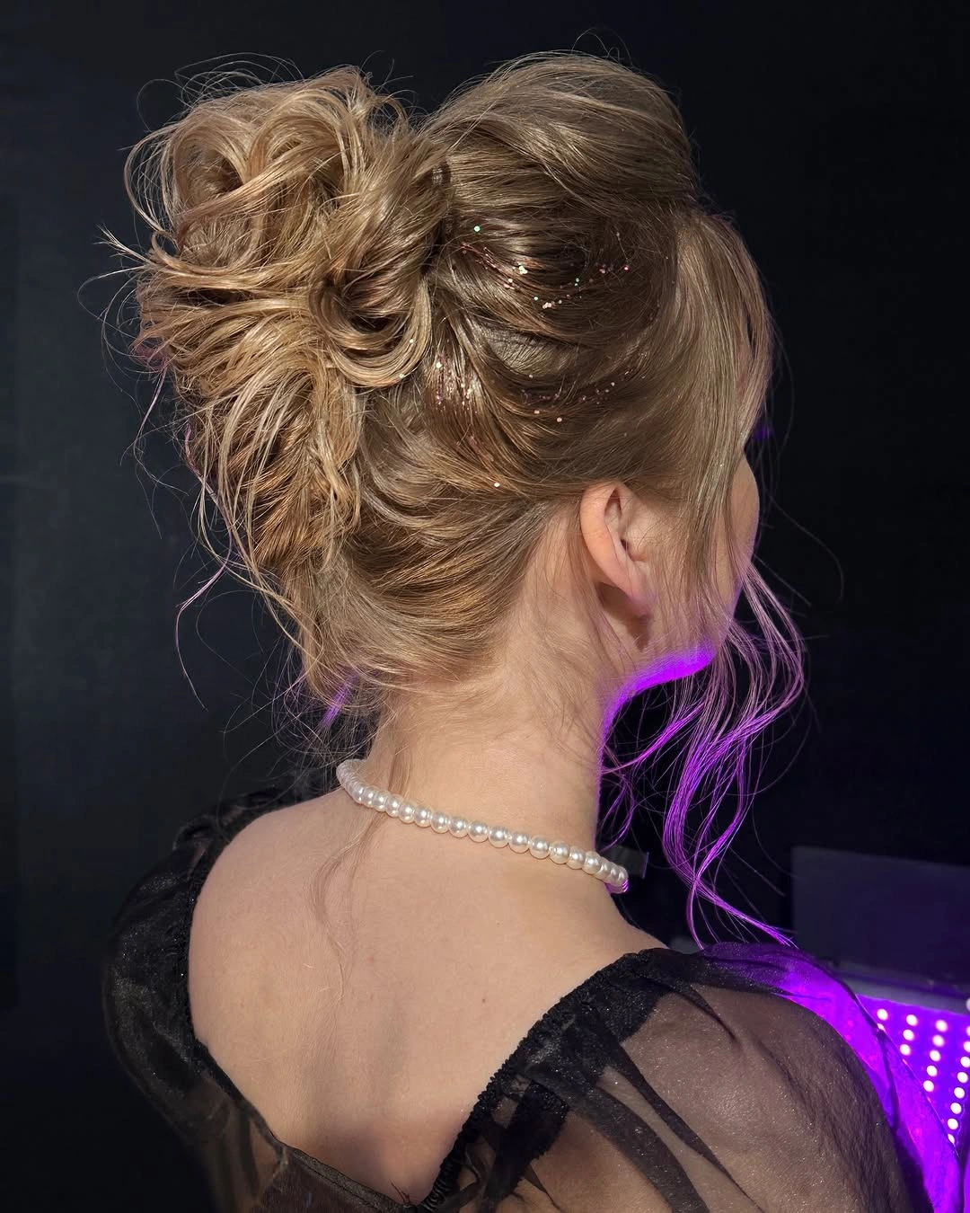 Blonde high updo with curled loops loose tendrils and reflective specks
