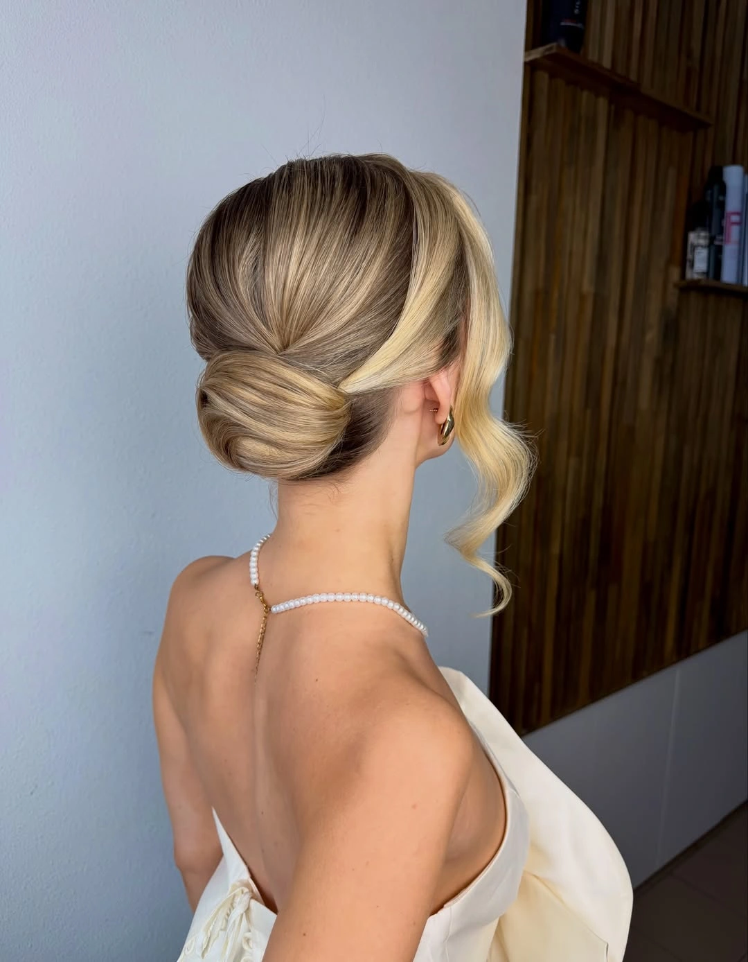 Blonde low chignon with smooth sweep and long curled face tendril