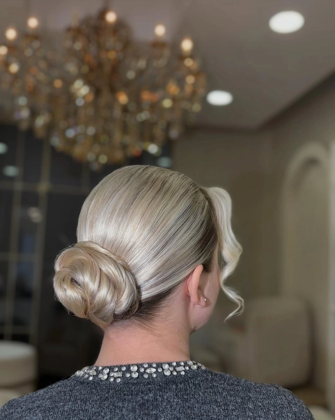 Pale blonde low bun with smooth sides and curled face tendril