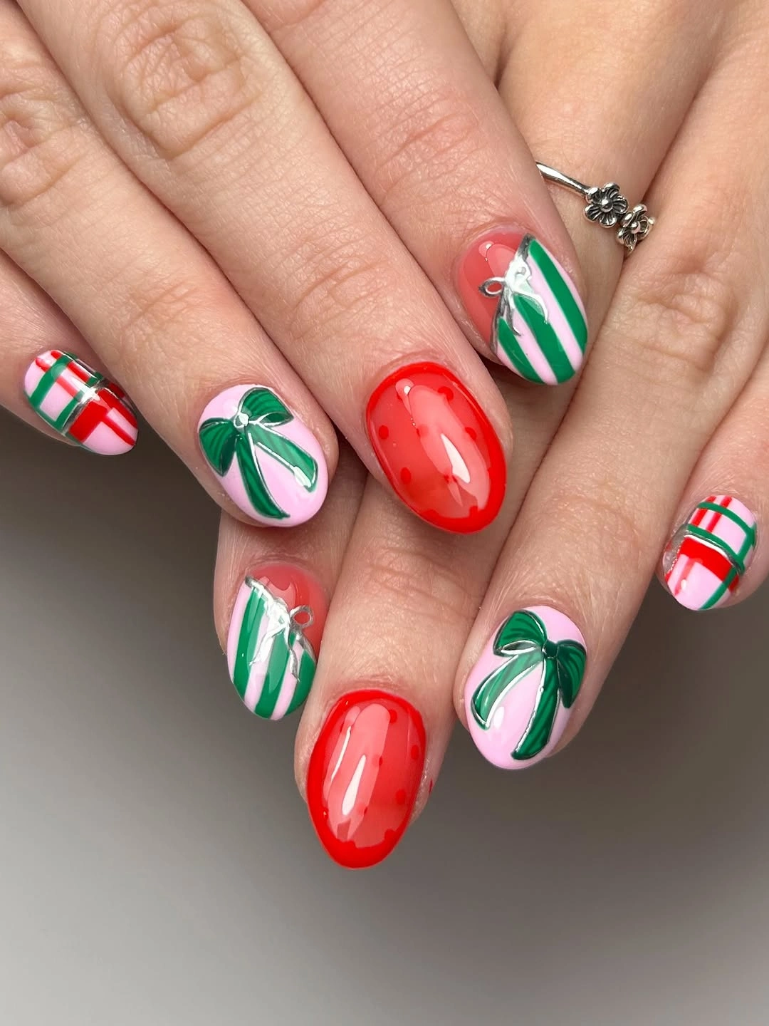 Short rounded nails with green bows, striped patterns, and glossy red accents