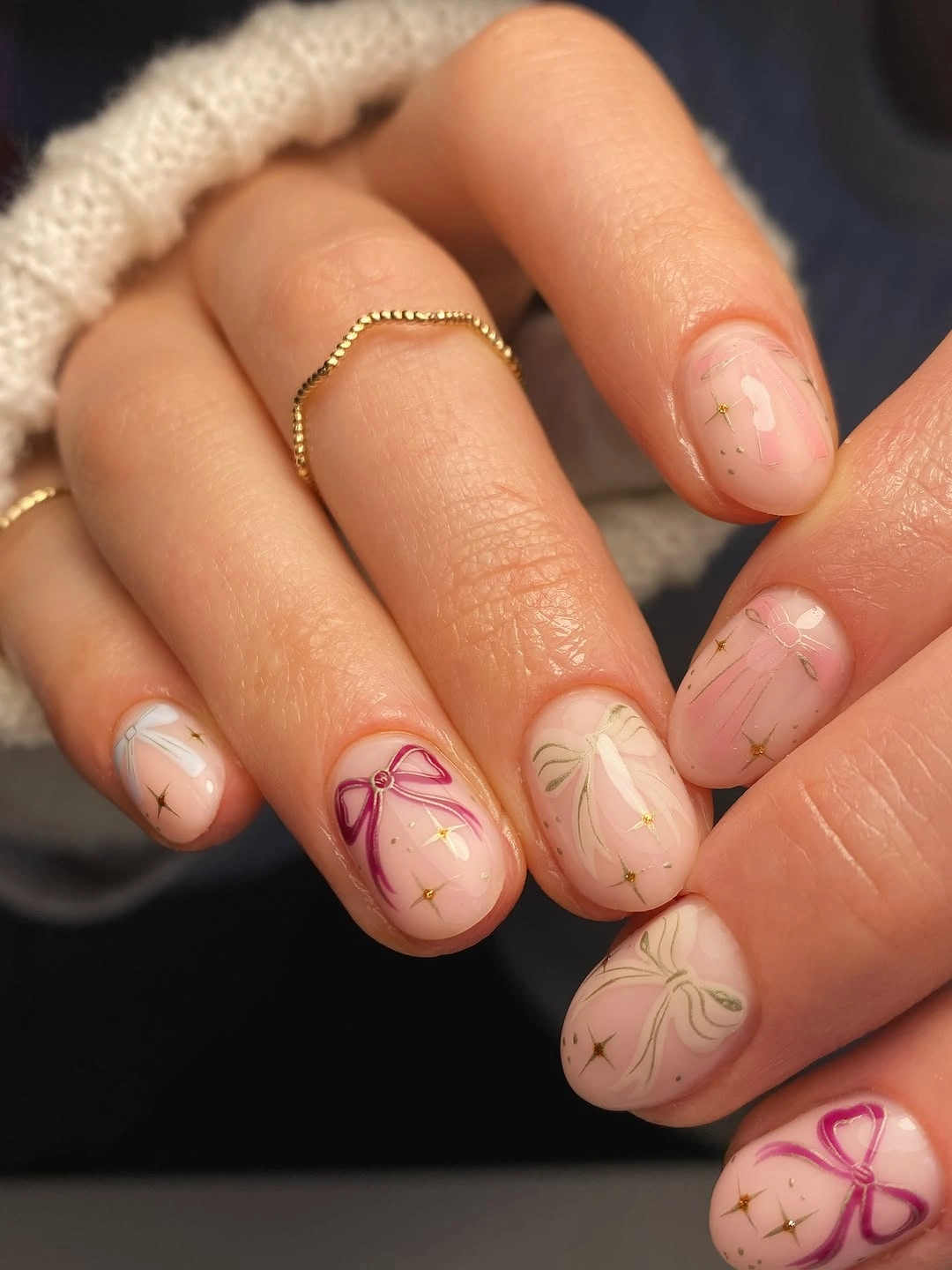 Short blush nude nails with pink, cream, sage bows, and gold starbursts