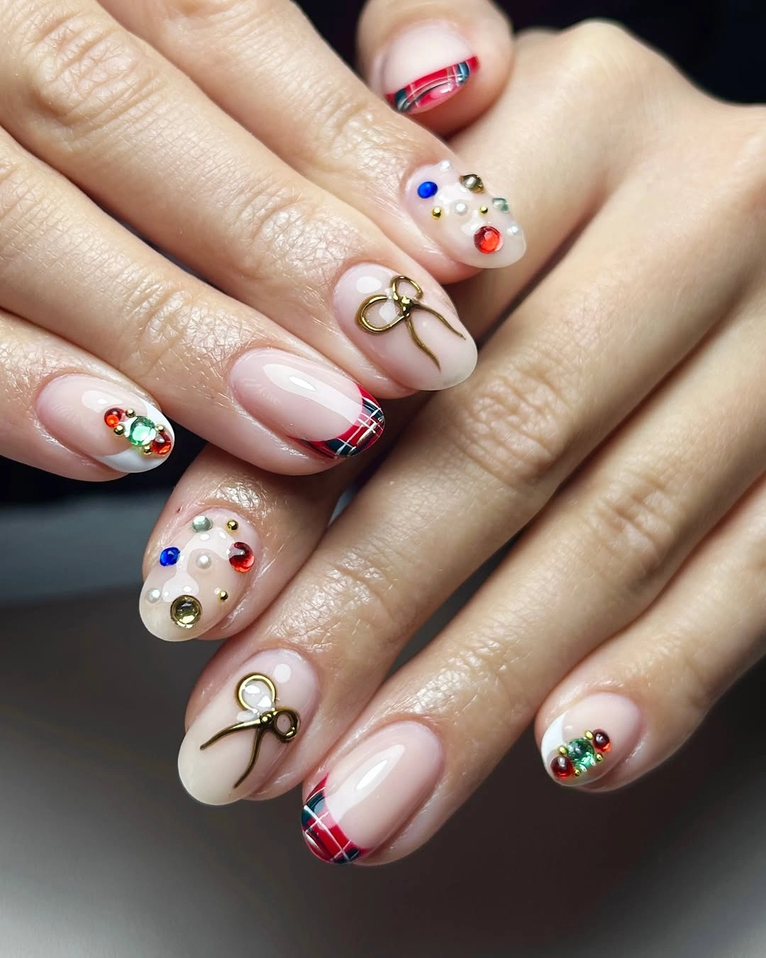 Nude pink nails with red plaid tips, gold bows, and multicolored gems