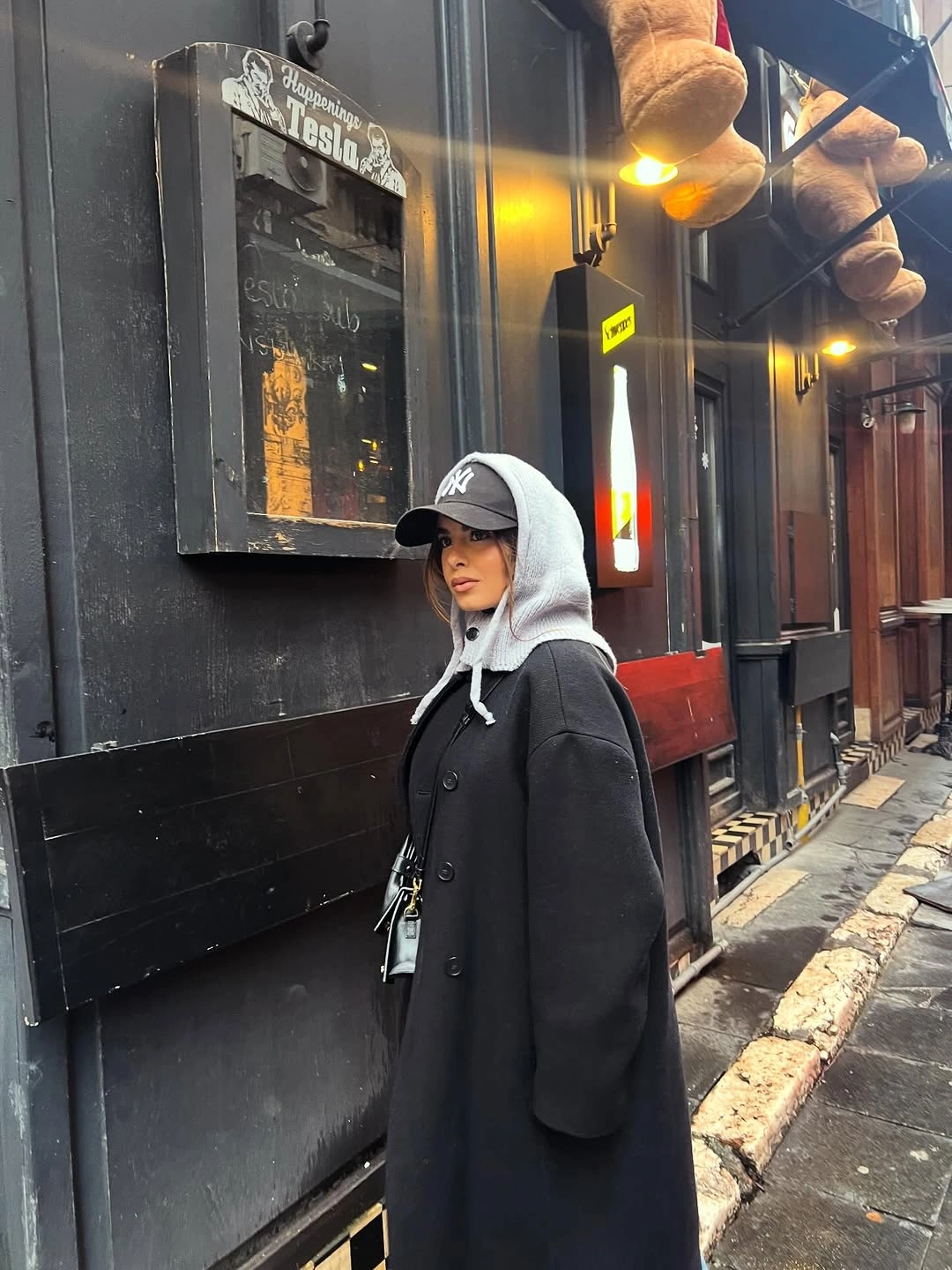Dark tailored coat over gray hoodie and black baseball cap