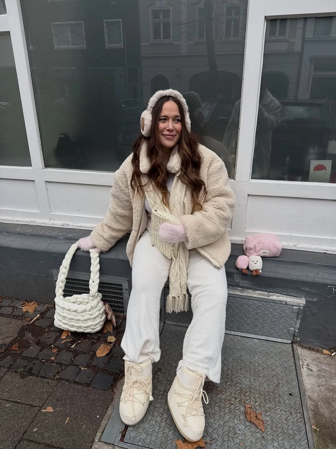 Cream textured jacket with white pants, earmuffs, scarf and pale boots