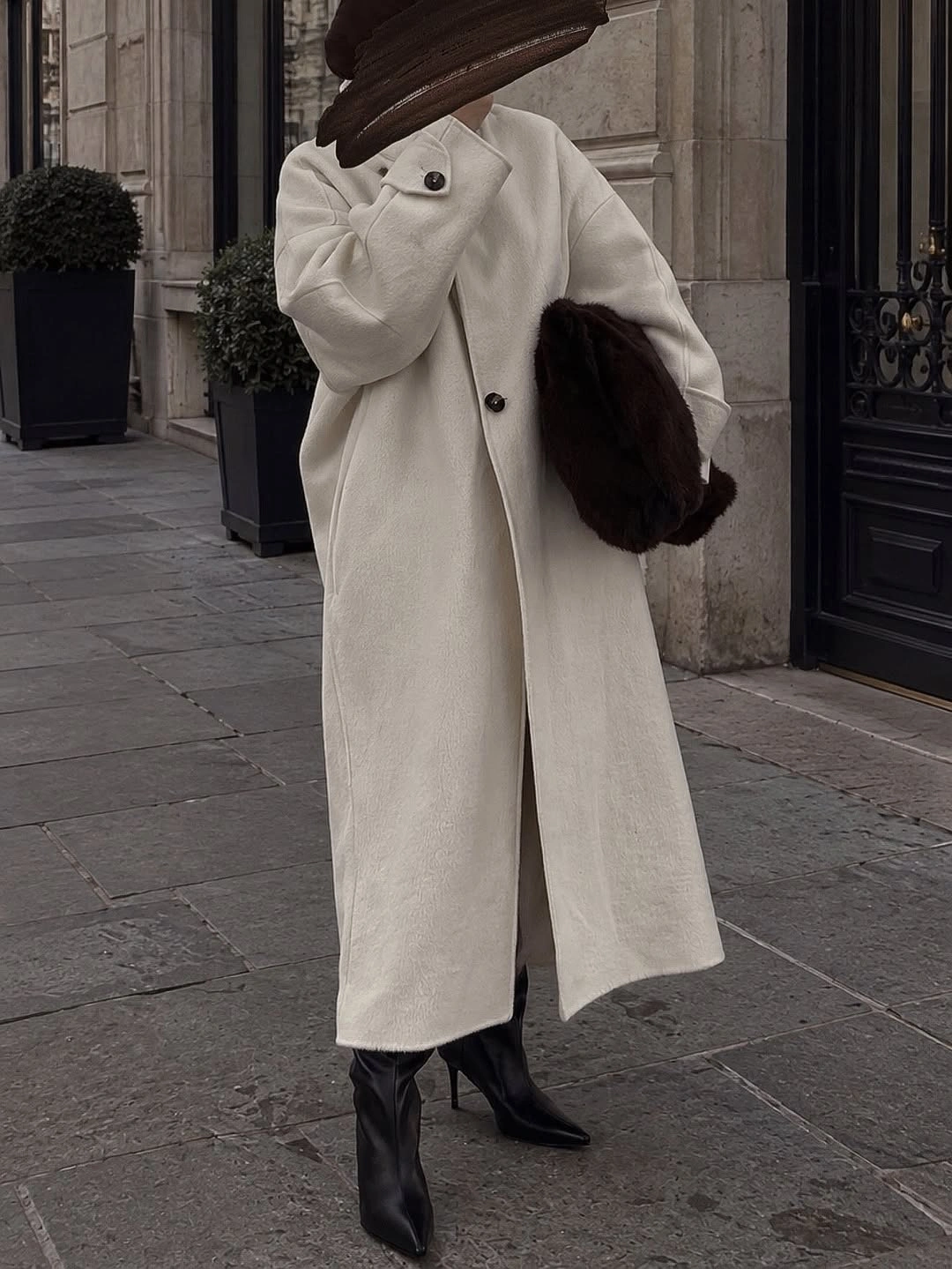 Long off-white coat with black pointed boots and brown textured bag