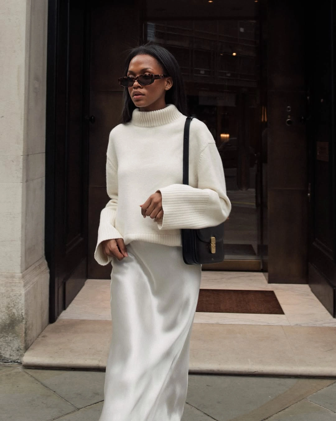 Cream turtleneck with long pale skirt and black shoulder bag
