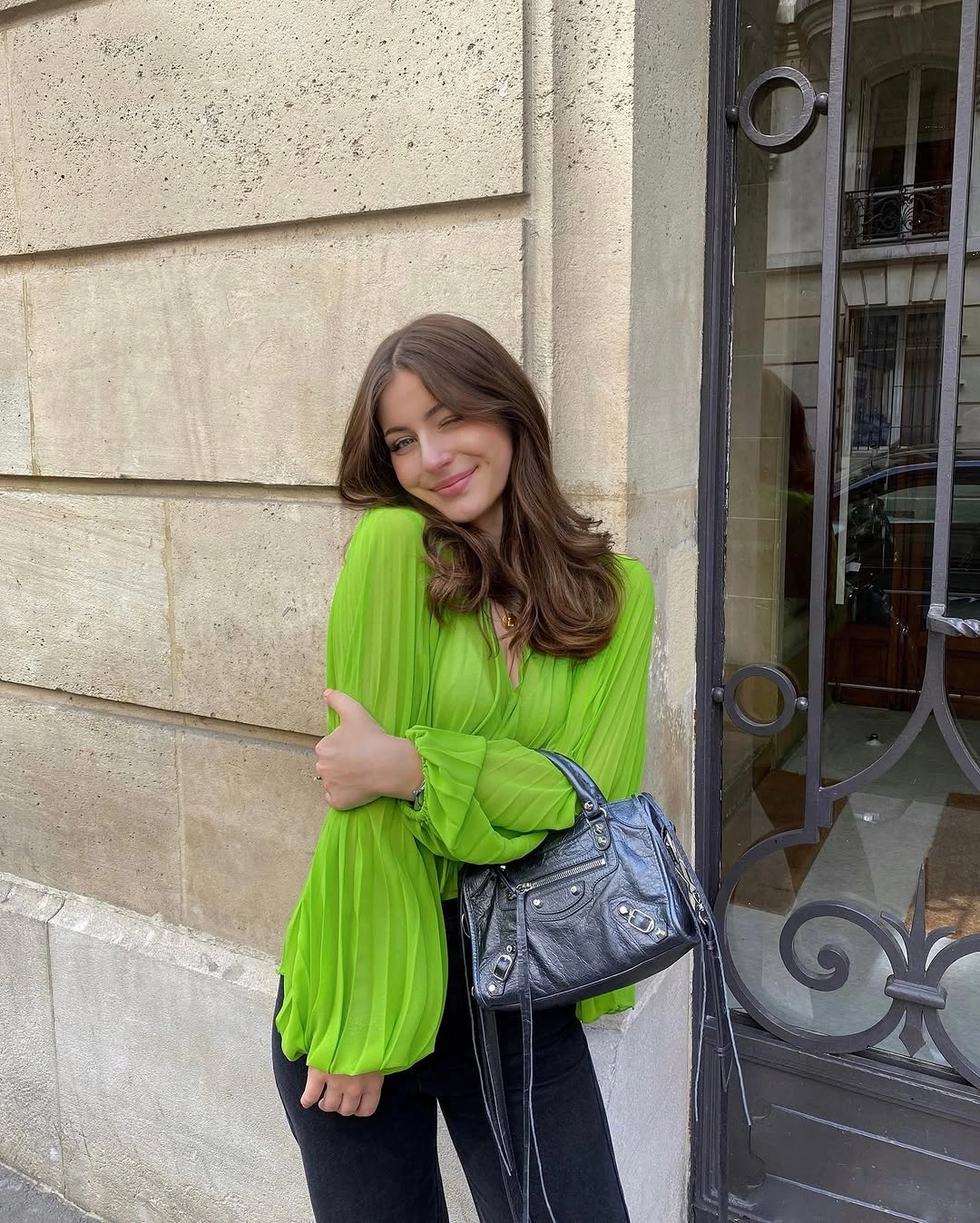 Bright lime-green pleated blouse with black trousers and gray structured handbag
