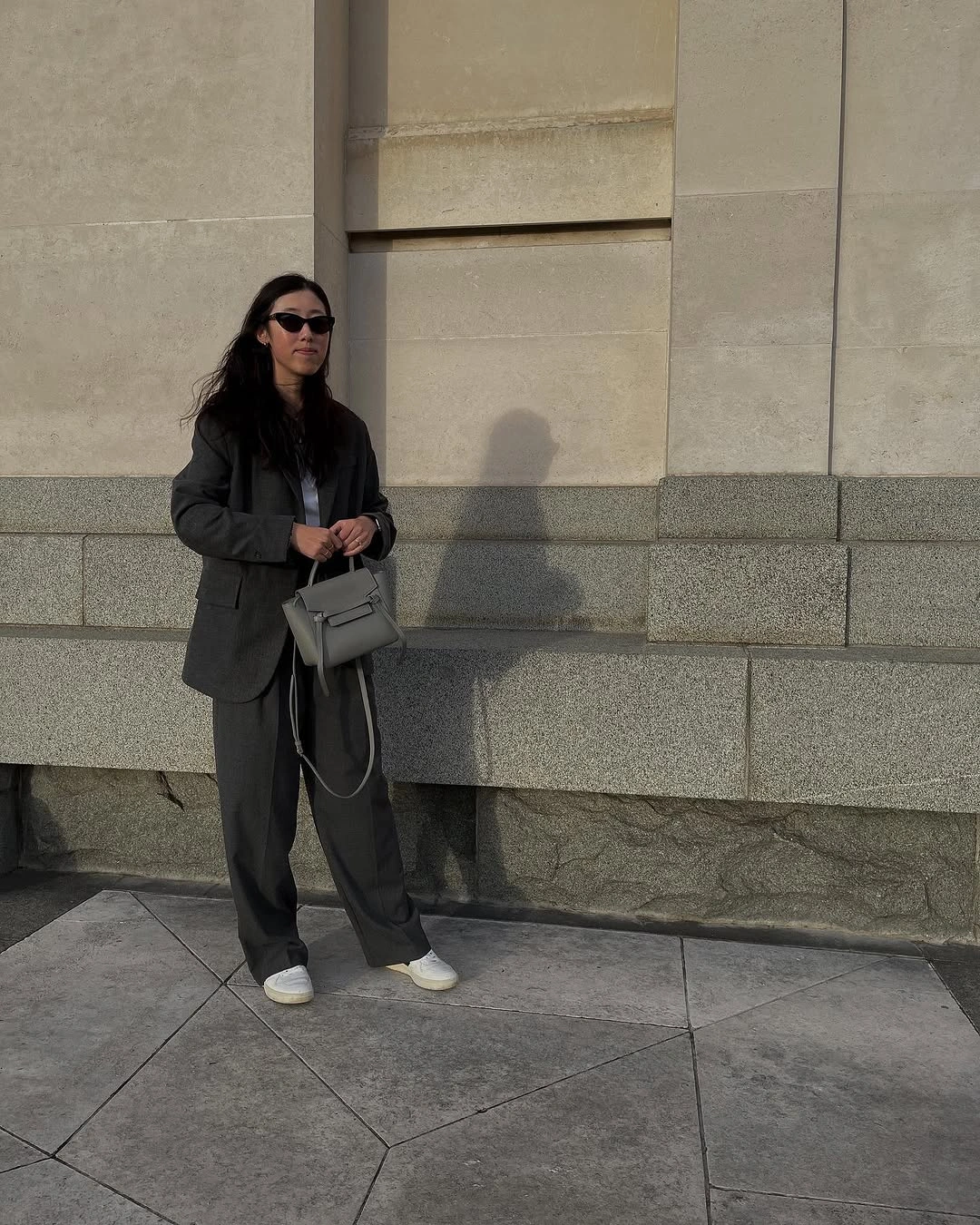 Oversized charcoal blazer with matching loose trousers, gray handbag, and white sneakers