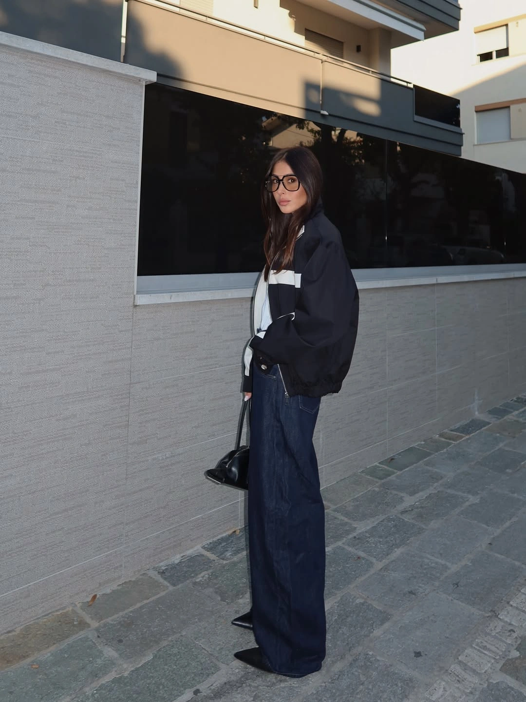 Dark oversized jacket with wide blue jeans, glasses, and black pointed shoes