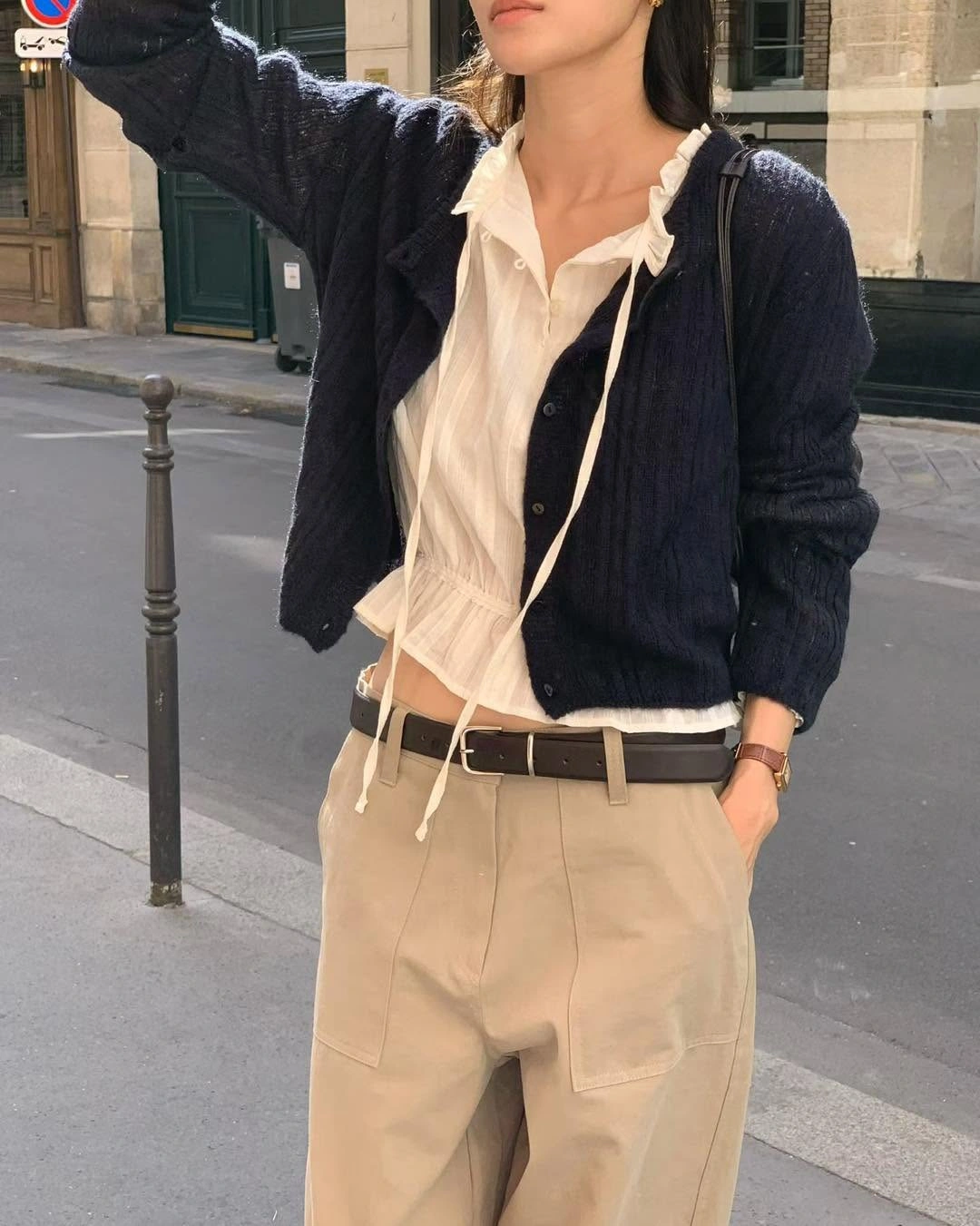 Navy cardigan over ruffled white blouse with beige trousers and dark belt