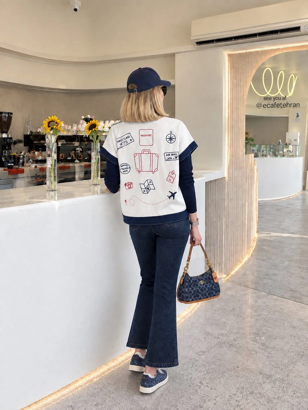 White graphic top over navy sleeves with flared jeans and baseball cap