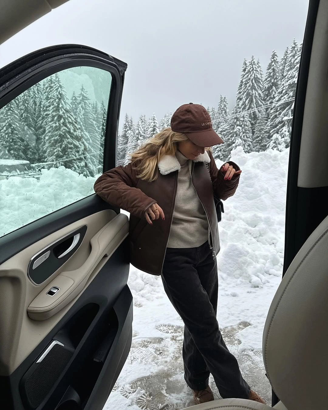 Brown jacket, gray sweatshirt, dark trousers, and baseball cap beside snow