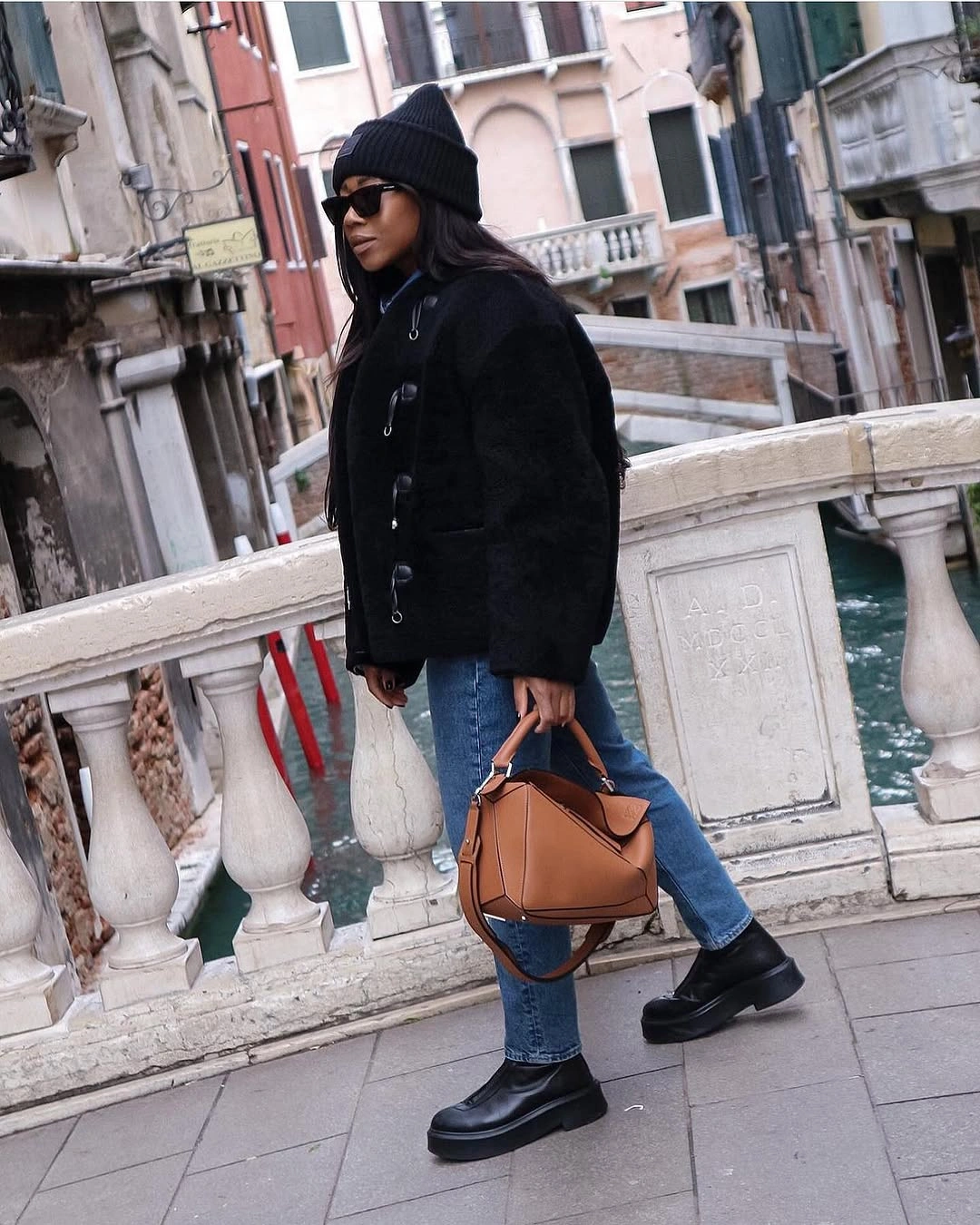 Boxy black jacket, cropped blue jeans, chunky black shoes, and tan handbag