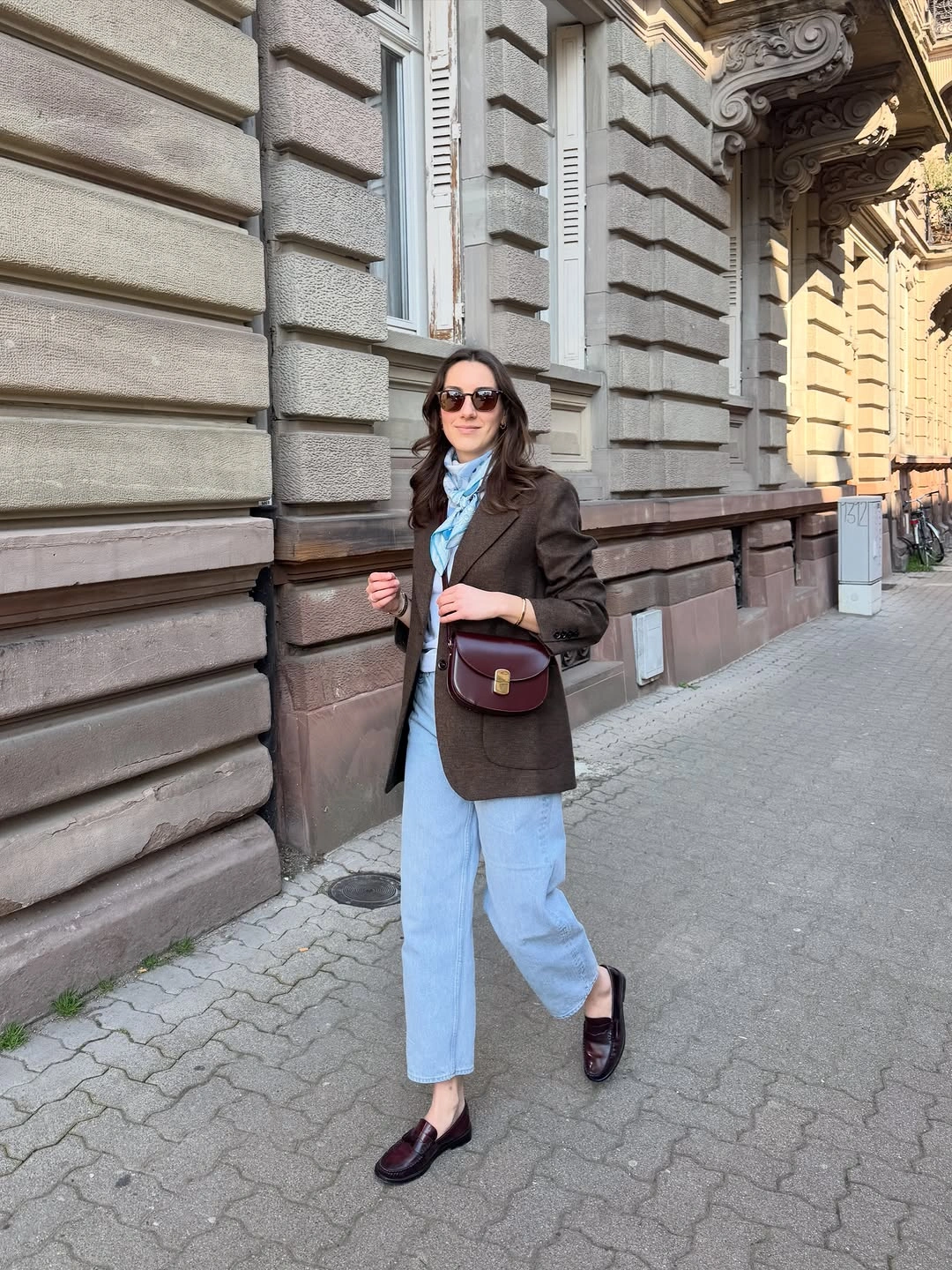 Brown blazer, pale blue jeans, blue scarf, burgundy bag, and loafers