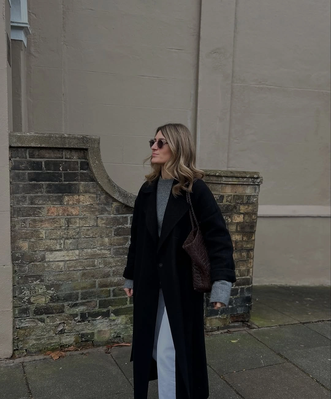 Long black coat over gray knit and pale blue trousers with shoulder bag