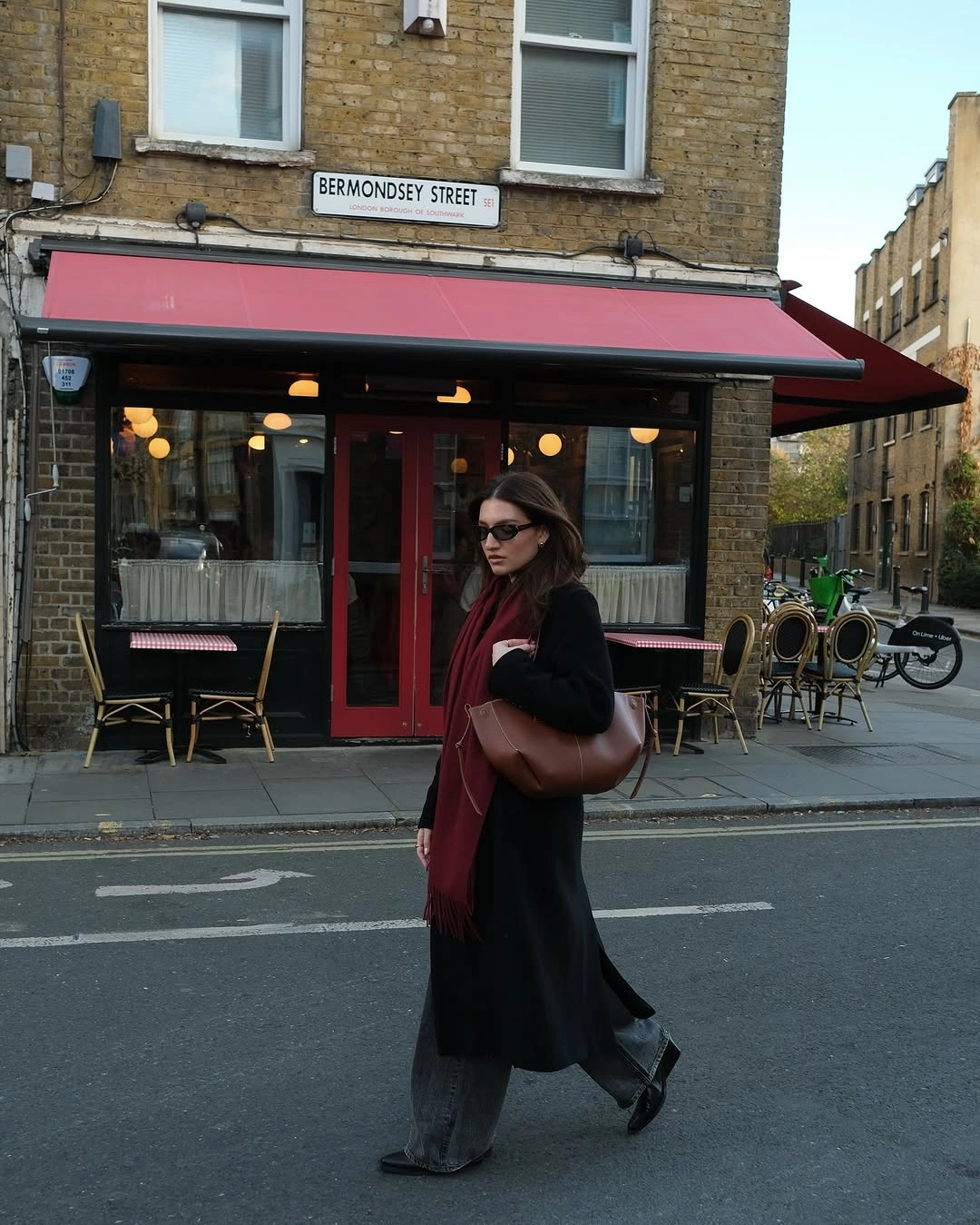 Black long coat with burgundy scarf, gray jeans, and brown bag