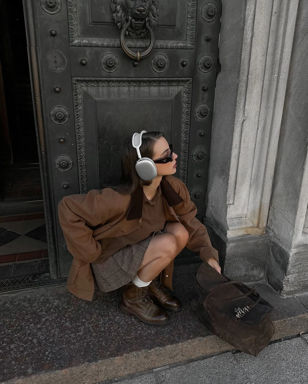 Brown oversized jacket, gray checked skirt, chunky boots, and silver headphones