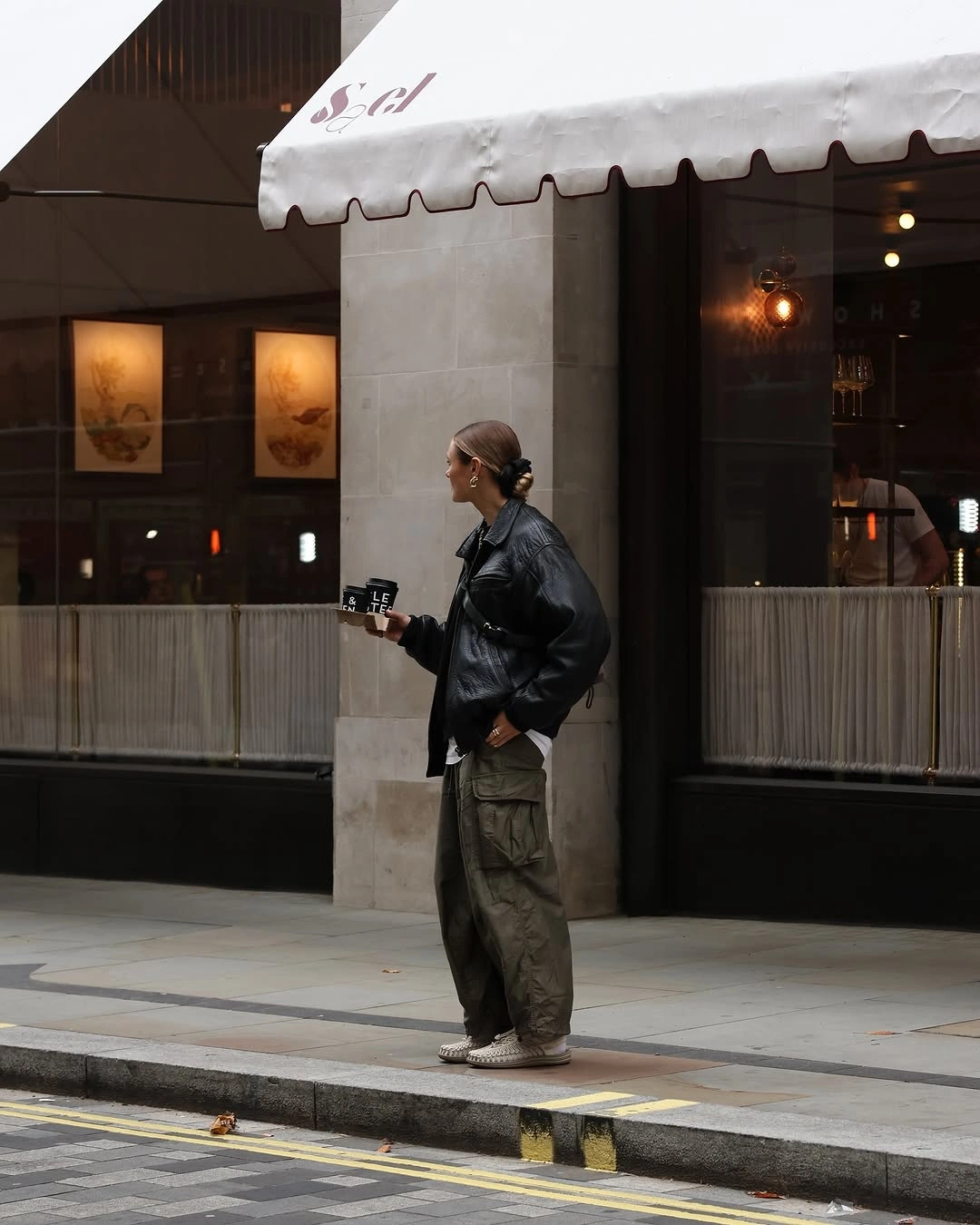 Oversized dark leather-look jacket, olive cargo trousers, and pale sneakers
