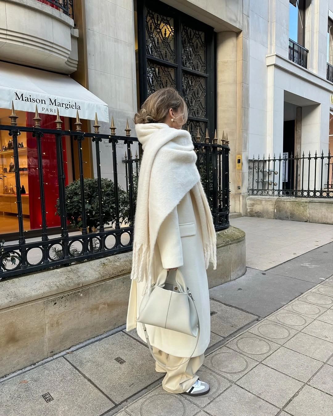 Long pale coat, oversized ivory scarf, cream trousers, and structured handbag