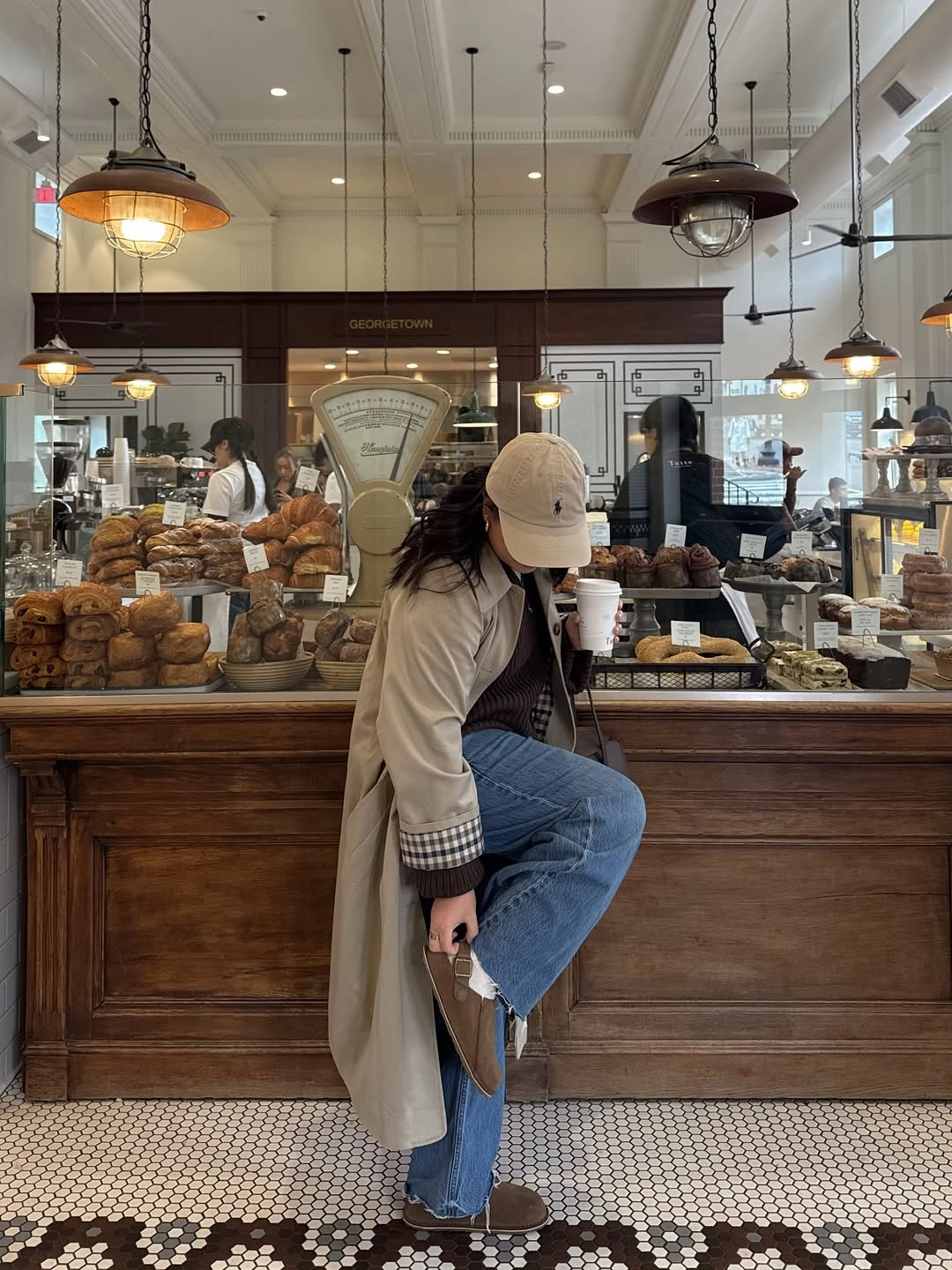Long beige trench coat, blue jeans, baseball cap, and checked cuffs
