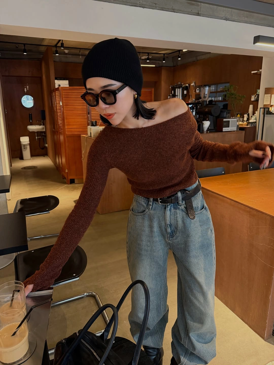 Brown off-shoulder sweater, loose blue jeans, black beanie, and dark handbag