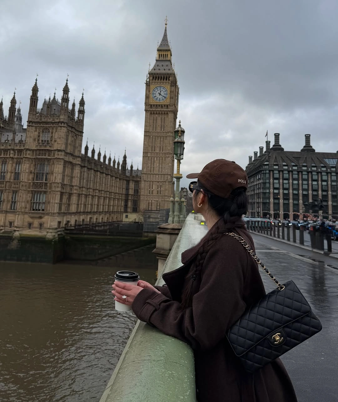 Long dark brown coat, brown baseball cap, and black quilted shoulder bag
