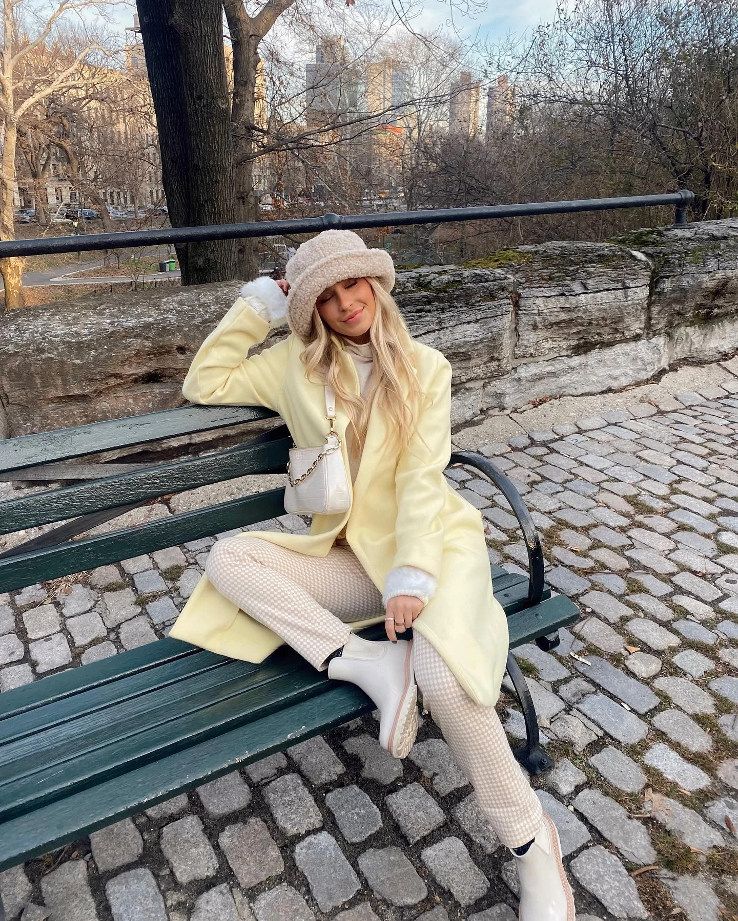 Pale yellow coat with cream hat, textured trousers, and light ankle boots