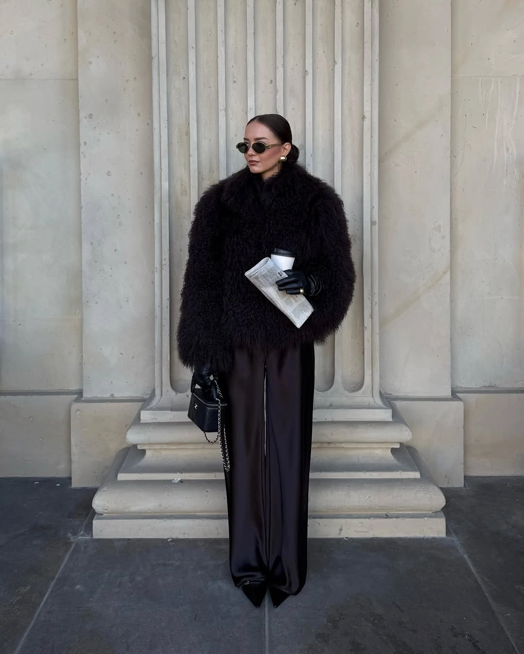 Black shaggy jacket with flowing dark trousers, sunglasses, gloves, and handbag