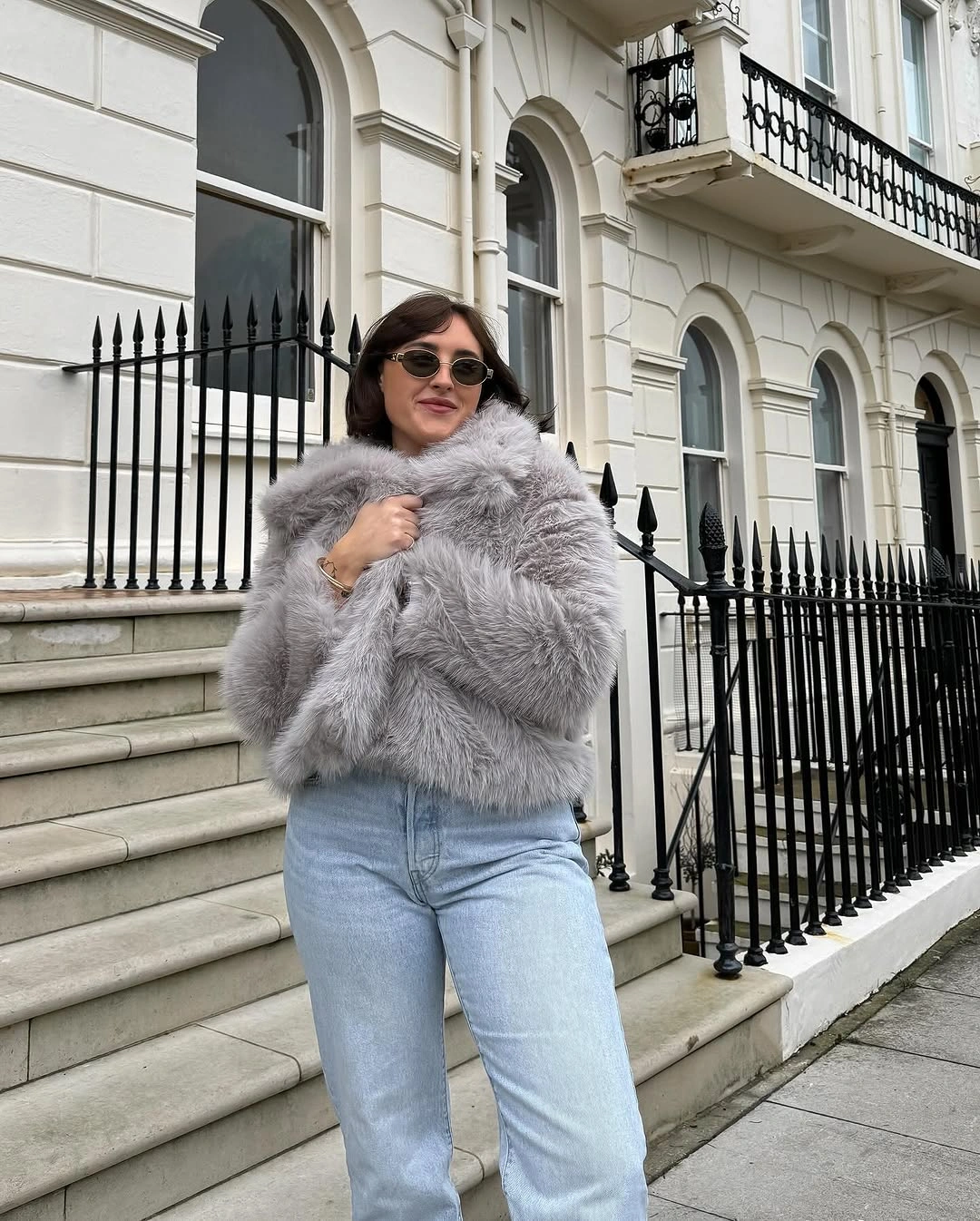 Short gray fluffy jacket with light blue jeans and round sunglasses