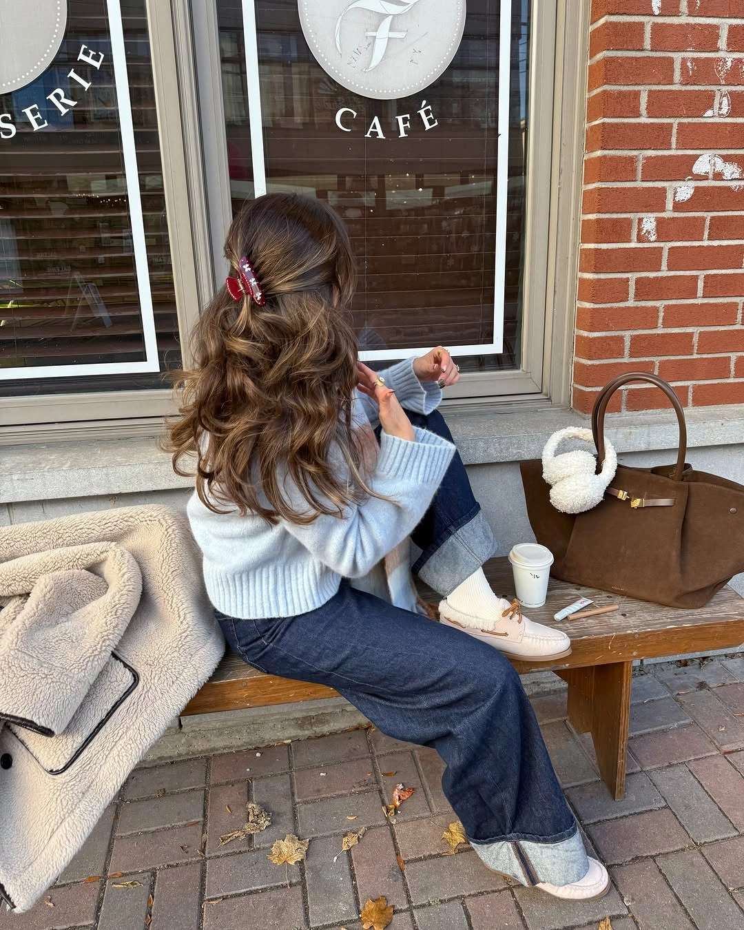Pale blue sweater with cuffed dark jeans, cream sneakers, and brown handbag