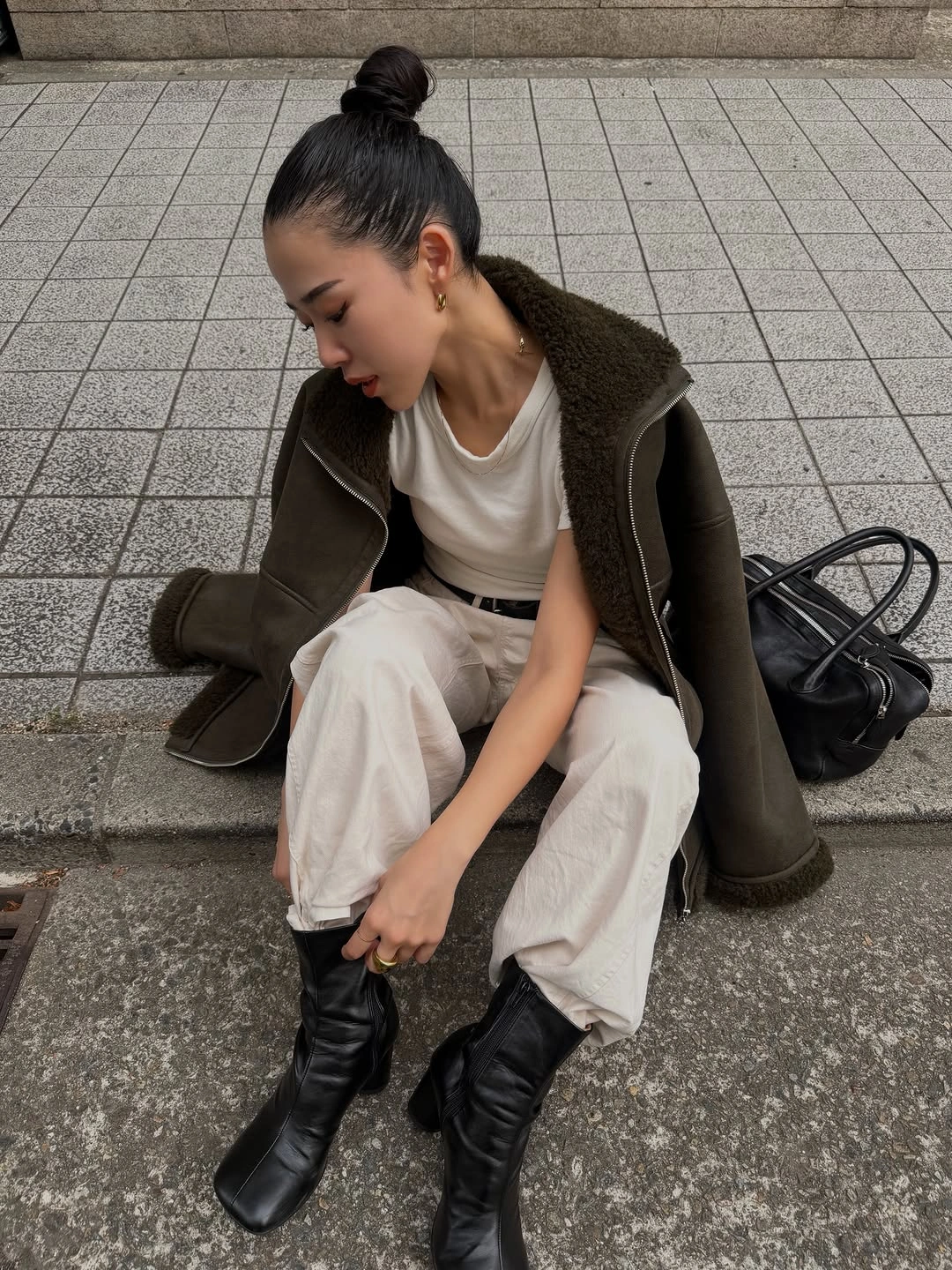 Dark olive jacket over white top and loose trousers with black boots