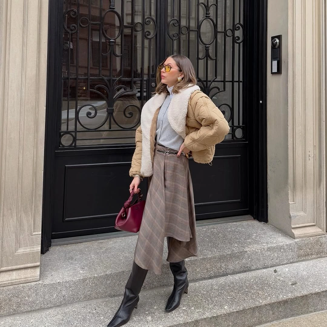 Tan quilted jacket with asymmetric plaid skirt, black boots, and burgundy handbag