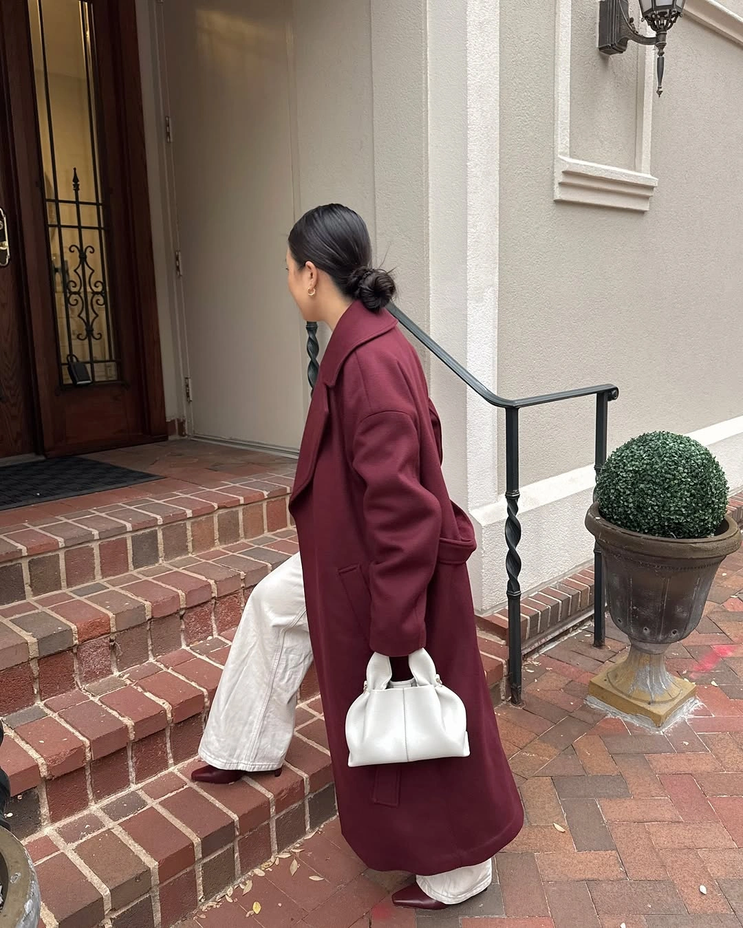 Long burgundy coat with loose white trousers and small white handbag