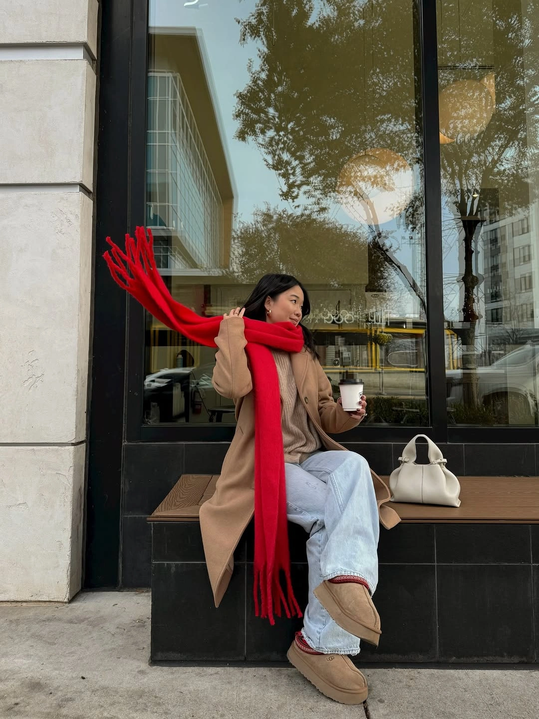 Camel coat with long bright red scarf, loose jeans, and tan shoes