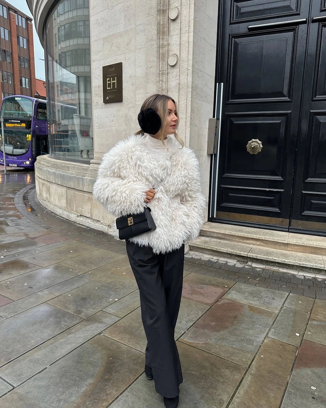 Shaggy white jacket with black earmuffs, dark wide trousers, and handbag