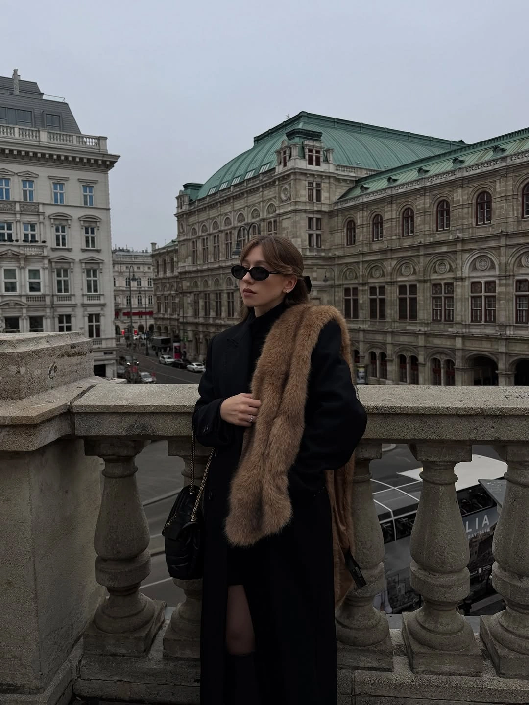 Long black coat with brown textured shoulder drape and dark sunglasses