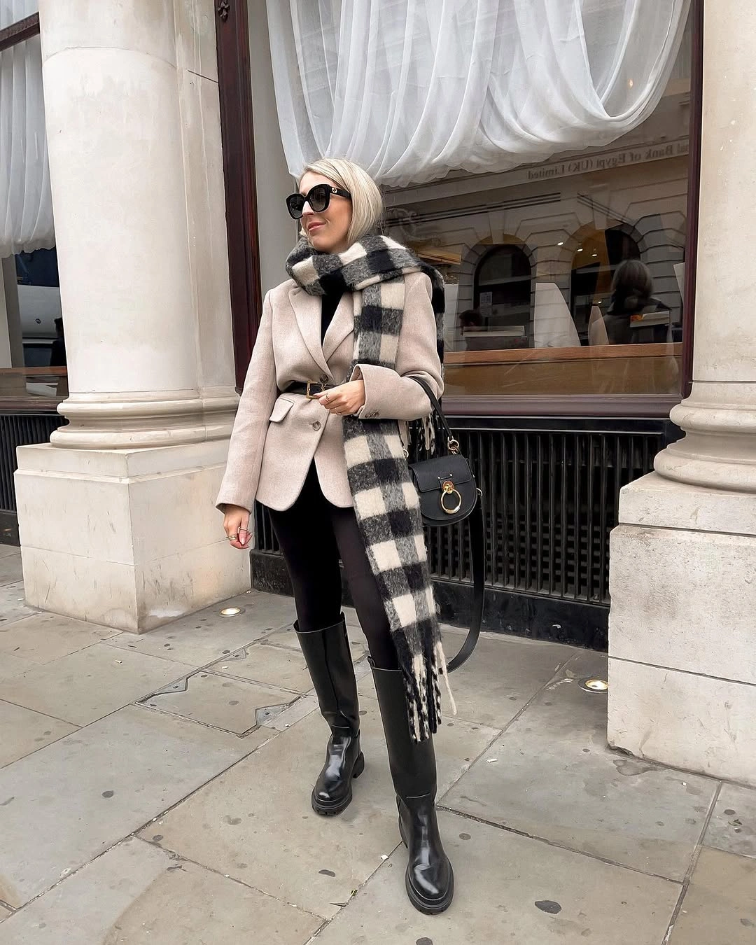 Beige structured jacket, long checked scarf, black pants, boots, and handbag.