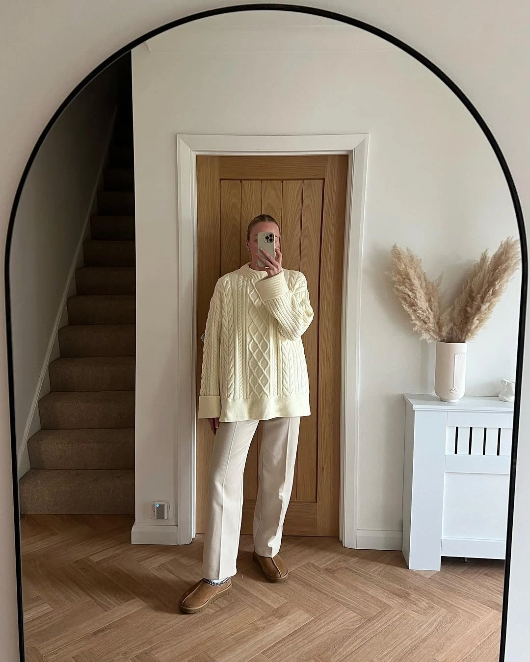 Oversized ivory cable-knit sweater, light cream pants, and tan rounded shoes.