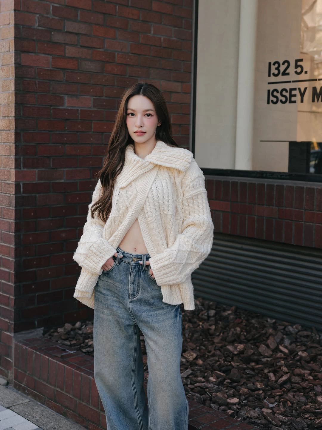 Cropped cream cable-textured knit with wrapped neckline detail and loose blue jeans.
