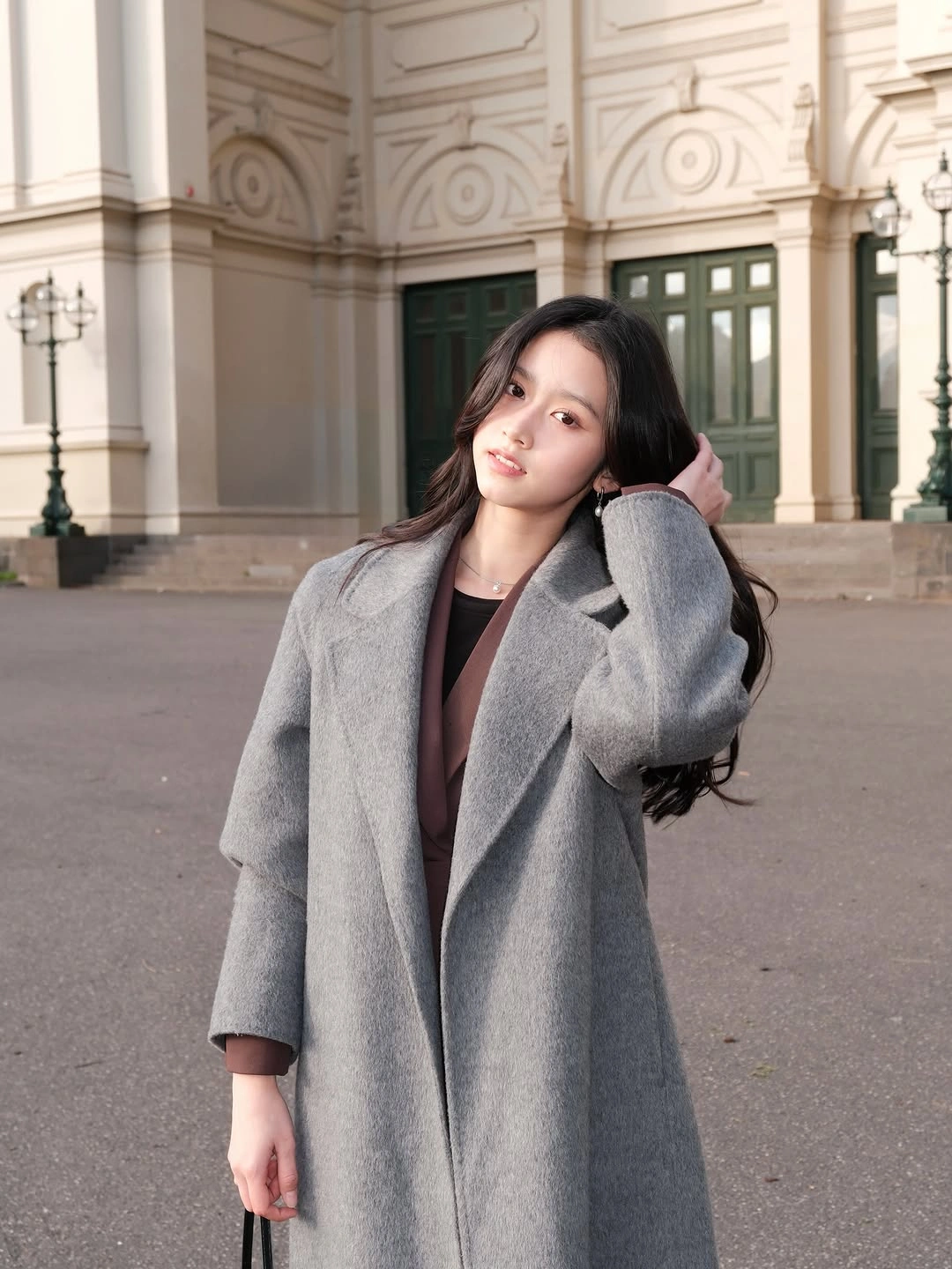 Oversized gray coat with broad lapels, dark brown neckline, and small jewelry.