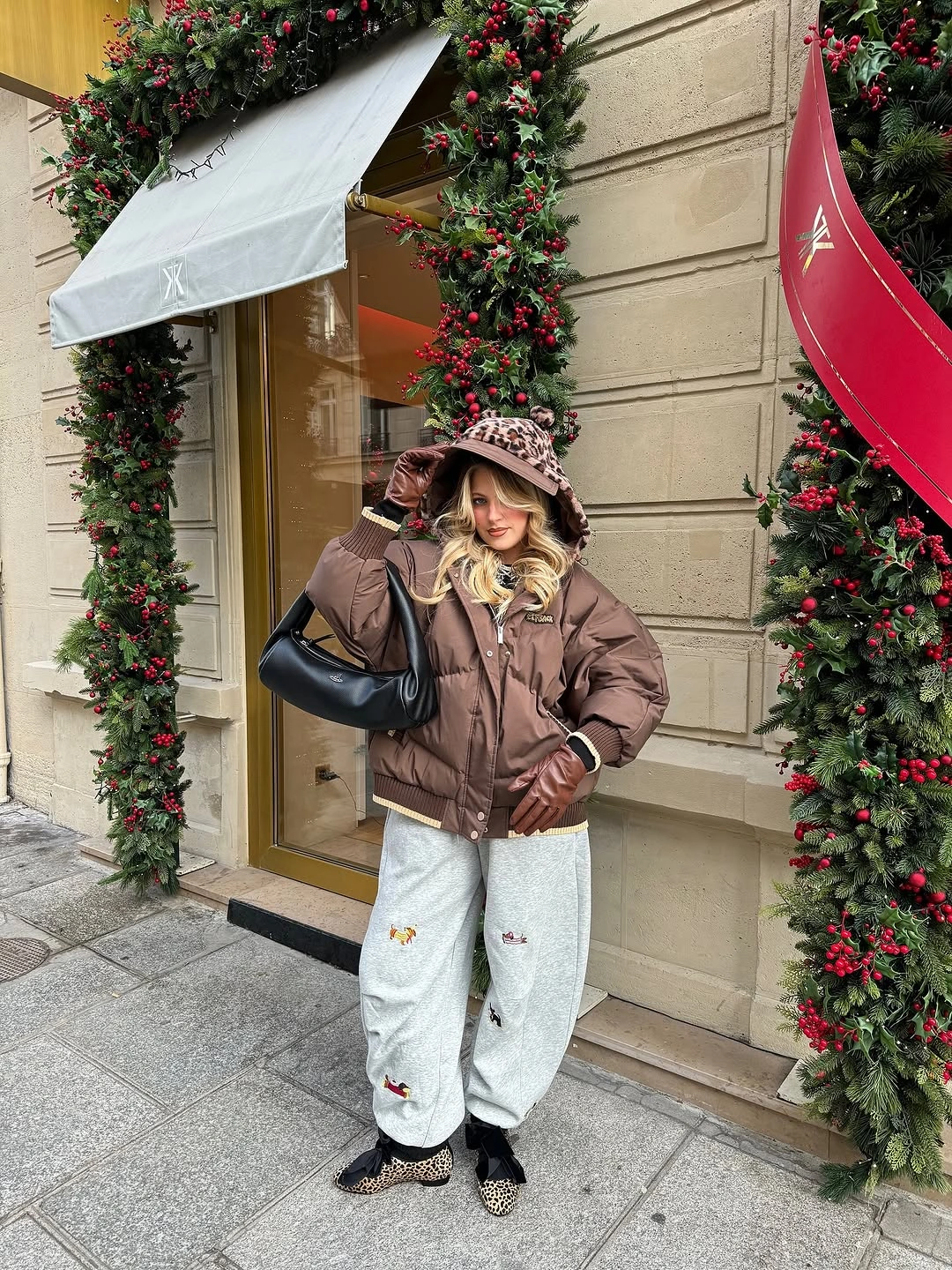 Brown puffer-style jacket, patterned hat, loose gray pants, and patterned shoes.