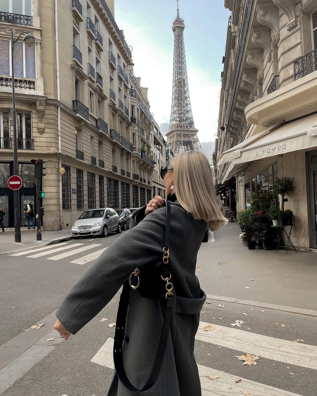 Long charcoal coat with wide sleeves, waist belt, and black shoulder bag.