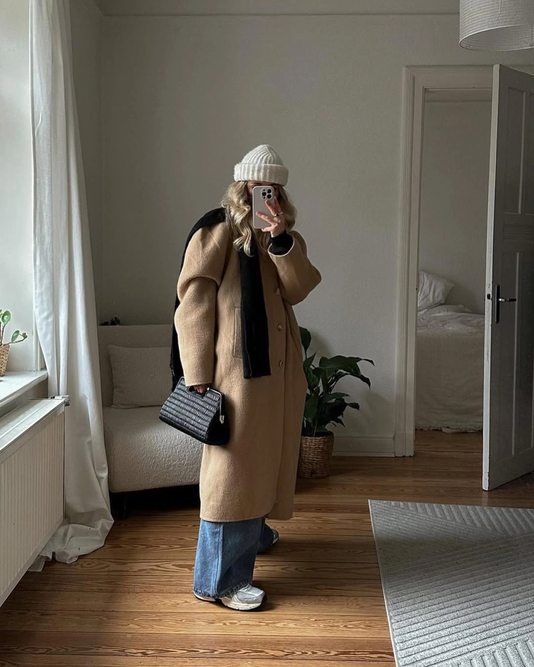 Long camel coat, black scarf and bag, cream beanie, wide jeans.