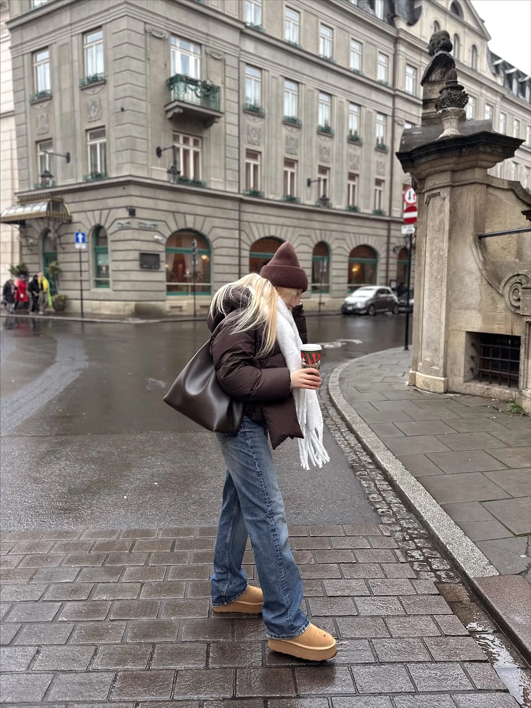 Brown puffer jacket, long white scarf, knit beanie, blue jeans, and tan shoes