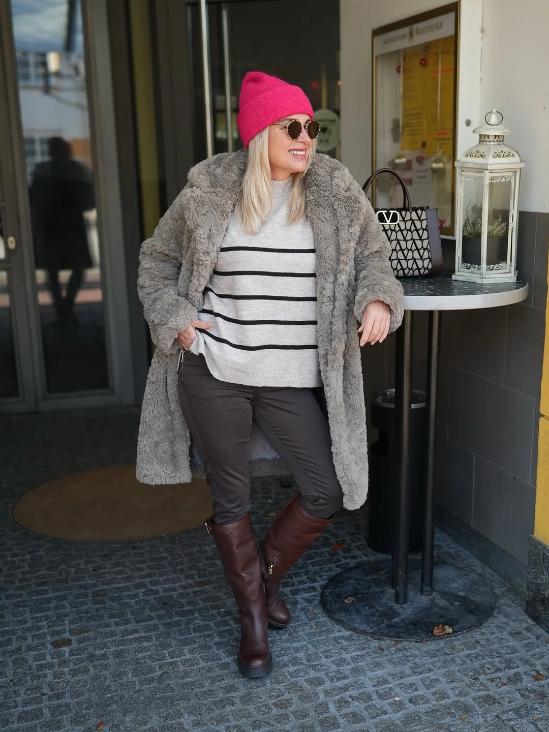 Gray textured long coat, striped sweater, pink beanie, and brown tall boots