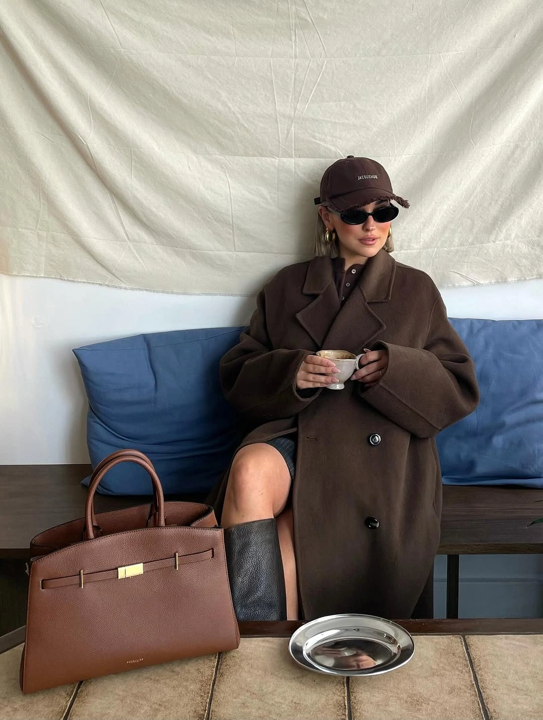 Dark brown oversized coat, baseball cap, sunglasses, and structured brown handbag